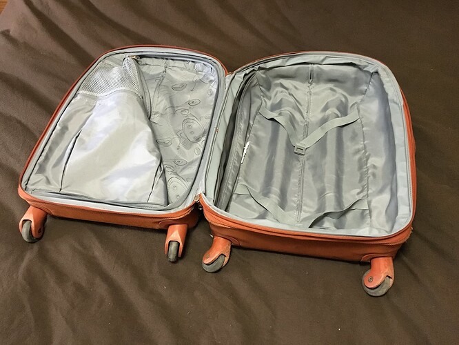 Orange carry on suitcase sits open and empty on a bedspread.