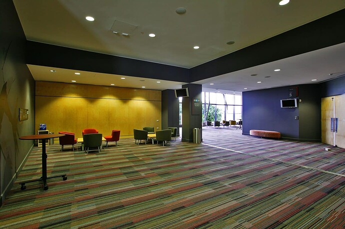 Open space of a conference center, with clusters of empty chairs under spotlights, blank screens, and no people in sight