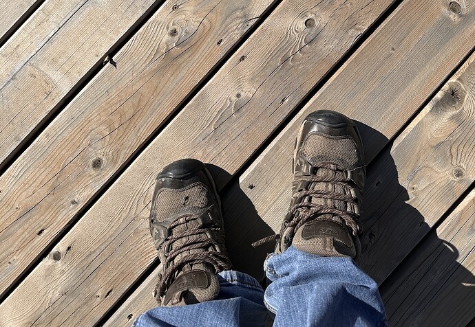 A pair of worn walking shoes stand on a wood deck ready to take 25 steps