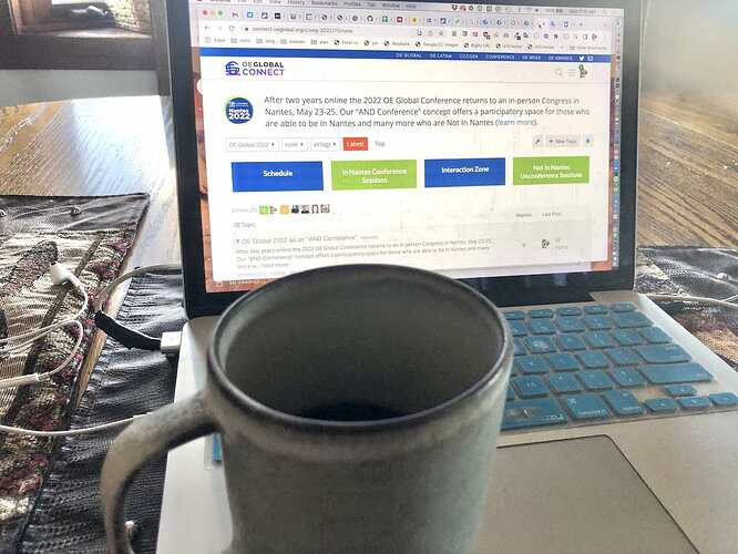 A mostly empty coffee cup in front of a laptop with the OEG Connect site for the conference