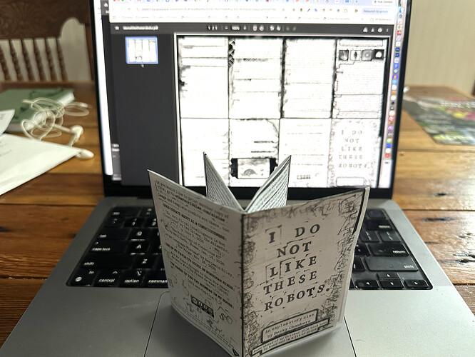 folded tiny multi page magazine title I do not Like these robots in front of a laptop displaying the PDF they were printed on