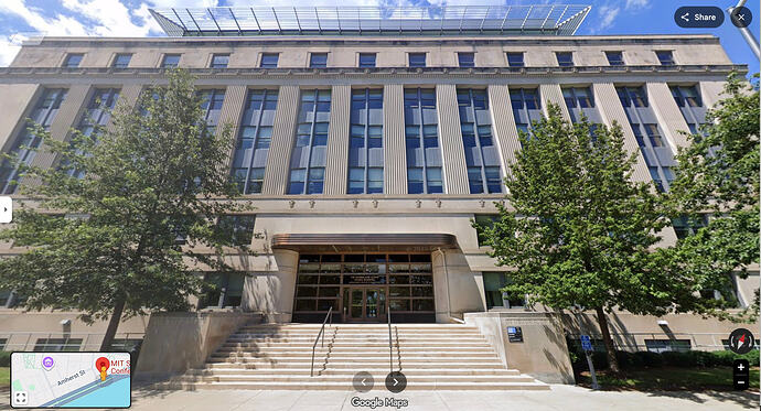 7 story art deco building with steps leading to the front doors, above are windows for the iddke floors. At the top is a hint of a metallic roof structure that is part of the conference center. Four tall green trees sit on both sides of the doors.