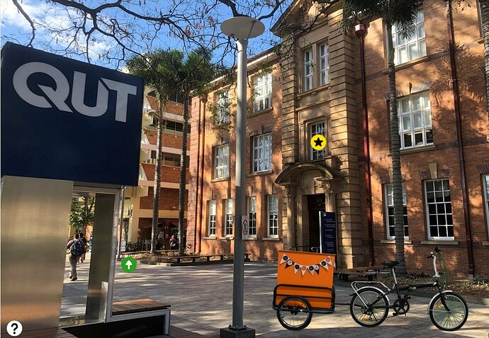 QUT open access bike pulling an orange trailer in front of a brick campus building