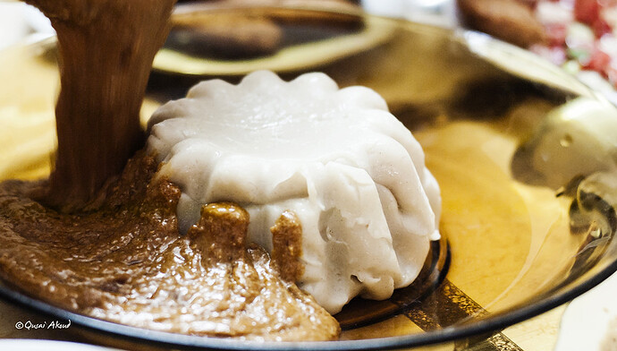 White mold-shaped item with brown sauce being poured on a gold plate.