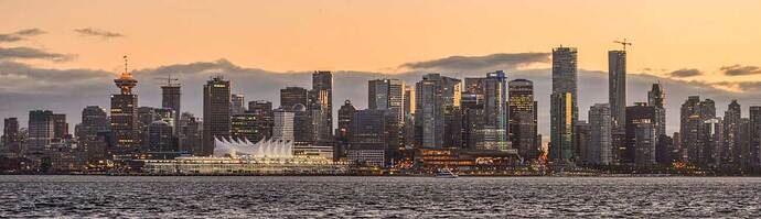 The tall buildings of Vancouver extending across the screen, seen from the water north of the city.