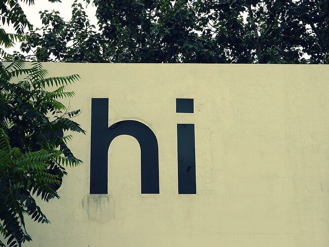Large dark “hi” lettering on a pale yellow wall, partly covered by green tree branches.