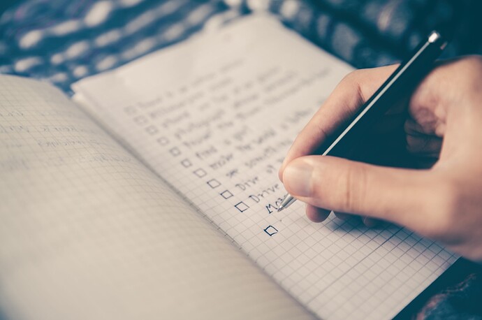hand holding a pen over a notebook with a list of items organized as a checklist