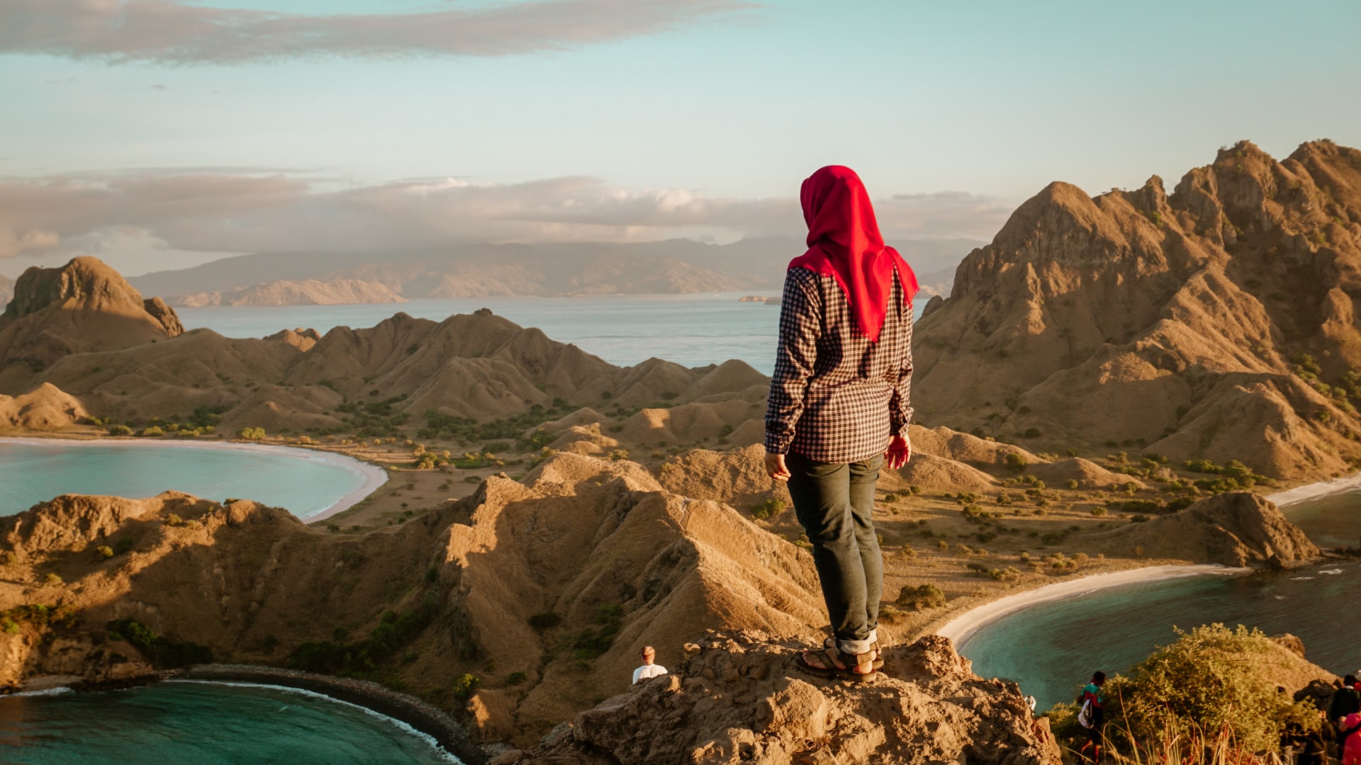 solitary woman in red headdress stands atop mountain peak overlooking lakes