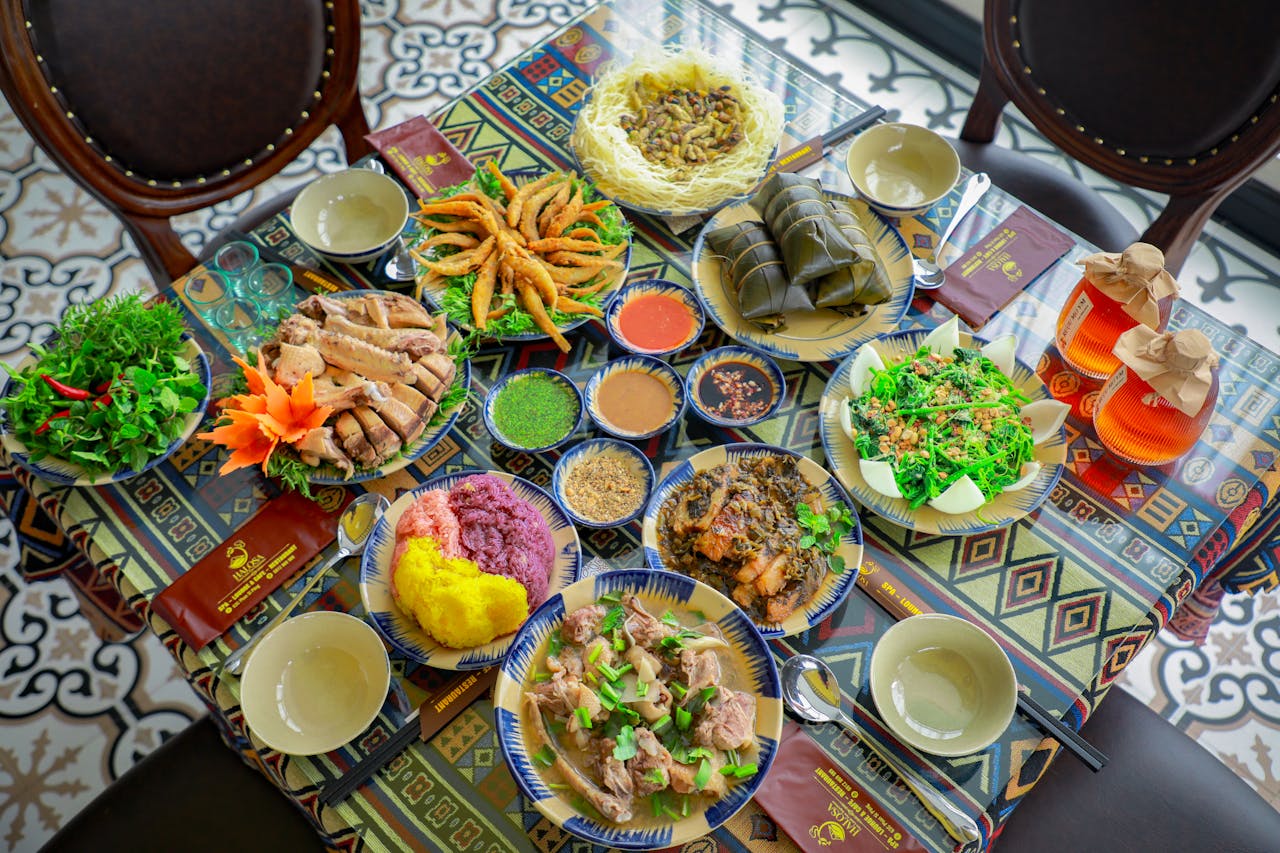 Dining table full of various sized color Asian style foods, many different colors and textures. Empty chairs are on eah side of the table. Each setting has a small bowl that looks too small to me!