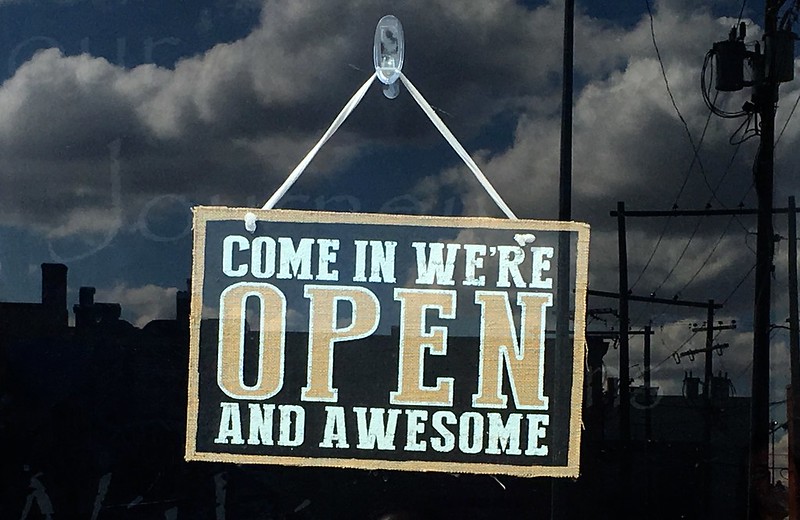 Sign hanging in a shop window reading- Come in, we're Open and Awesome